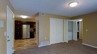 This single-floor residential unit offers a practical and well-organized layout designed for comfortable everyday living. The open living area is finished with plush wall-to-wall carpeting, creating a warm and inviting atmosphere, while the adjacent kitchen transitions to durable tile flooring. The kitchen is outfitted with dark espresso cabinetry, stainless steel appliances including a full-size refrigerator, microwave, and range, providing a functional and stylish cooking space. A thermostat is conveniently positioned on the central wall, allowing easy climate control throughout the unit. The space includes a set of bifold closet doors offering generous storage, ideal for linens or general organization. A dedicated in-unit laundry area is tucked neatly to one side, housing a full-size washer and dryer — a practical convenience that adds significant value. The textured ceilings and flush-mount lighting fixtures are consistent throughout, contributing to a cohesive interior aesthetic. Overall, the unit delivers a straightforward, functional design with thoughtful storage solutions and essential modern amenities all contained within a single level.