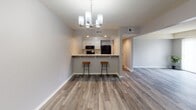 Located at 6014 Meadows Dr in Fort Wayne, Indiana, this single-floor residence offers a thoughtfully updated interior with a cohesive, modern aesthetic throughout. The open-concept living and dining area features wood-look vinyl plank flooring and a stylish chandelier that anchors the space with warm, ambient light. A smooth transition leads into the kitchen, which is separated by a peninsula counter topped with marble-look quartz surfaces and equipped with bar seating for two. The kitchen itself is outfitted with white cabinetry, matching quartz countertops, a subway tile backsplash, and black stainless appliances including a gas range with an overhead microwave. The dining area flows into a hallway connecting the rest of the unit, where two carpeted bedrooms provide a quiet, comfortable retreat. Each bedroom features neutral gray walls, vertical blind-covered windows with outdoor views, and generous closet space. The unit includes two bathrooms: a full bath with a wide vanity, warm wood cabinetry, a large mirror, and shower access; and a second bath featuring a single-sink vanity and a tub-shower combination with a decorative curtain. Wood-look flooring carries through the wet areas, reinforcing the home's consistent, updated character.