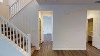 This well-appointed two-story residence combines modern finishes with a functional, open layout. The main level is anchored by rich, dark hardwood-style flooring that flows continuously through the entryway and hallway, creating a cohesive and inviting atmosphere throughout the space. Bright white walls and white trim work together to reflect natural and artificial light, lending the interior a clean, airy feel.

The entryway opens into a spacious corridor that leads toward a paneled white front door, providing a welcoming first impression. Recessed lighting in the hallway ensures the space remains well-lit and practical. Adjacent to the entry, a staircase with white-painted balusters and a classic newel post leads to the upper level, with carpeted treads offering a comfortable contrast to the hard flooring below.

The upper floor expands on the home's accessible and organized design, offering additional living space above. Throughout both levels, neutral tones and understated finishes create a versatile backdrop that accommodates a wide range of interior design styles. The overall ambiance is fresh, modern, and move-in ready, reflecting thoughtful attention to detail in both materials and layout.