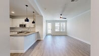 Located at 201 Hills Rd in Panama City Beach, FL, this thoughtfully designed single-floor unit offers a clean, modern aesthetic throughout. Light-toned luxury vinyl plank flooring runs continuously across the space, creating a cohesive and airy feel. Crown molding accents the ceilings, adding a refined architectural detail to each room.

The open-concept kitchen and living area serves as the heart of the unit. The kitchen is outfitted with crisp white shaker-style cabinetry, grey quartz countertops, a subway tile backsplash, and stainless steel appliances including a French door refrigerator, microwave, and range. A peninsula with pendant lighting provides additional counter space and defines the transition into the living area. The living room is bright and inviting, featuring a ceiling fan and windows with exterior views that bring in natural light.

The bathroom is finished with a sleek frameless glass sliding shower enclosure and white tile surround, complemented by wood-look flooring and neutral walls for a clean, spa-like feel. A dedicated laundry area houses a stacked washer and dryer unit, offering practical convenience within the footprint of the space. The overall design balances functionality with modern style in an efficient and well-appointed layout.