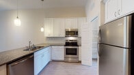 Located at 5500 Main St in New Port Richey, Florida, this single-floor residence offers a well-designed layout with clean, modern finishes throughout. The open-concept living area is bright and airy, featuring light wood-look flooring and a ceiling fan, with a clear sightline into the kitchen that makes the space feel expansive and connected.

The kitchen is thoughtfully appointed with white shaker-style cabinetry extending to the ceiling for generous storage, dark granite countertops, a subway tile backsplash, and a full suite of stainless steel appliances including a range, microwave, dishwasher, and refrigerator. Pendant lighting adds a warm accent, and a walk-in pantry provides additional storage convenience.

The bedrooms are carpeted and feature neutral walls with ample natural light from windows fitted with blinds. A spacious walk-in closet with wire shelving systems offers well-organized storage. The primary bathroom includes a large walk-in shower with white subway tile, a mosaic accent border, sliding glass doors, and a white vanity with stone countertops. A second full bathroom features a tub-shower combination with matching tile detailing and a similarly styled vanity, complemented by light tile flooring throughout.