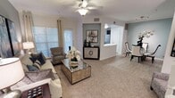 This two-story residence offers a thoughtfully designed layout that balances comfort and functionality. The living area is a welcoming centerpiece, featuring plush carpeting, crown molding, and a ceiling fan that enhances airflow and ambiance. Large windows dressed with grommet curtains invite generous natural light while maintaining privacy, creating a bright and airy atmosphere throughout the day.

An accent wall with a built-in console niche adds a decorative focal point to the living space, lending architectural character to the room. The open-concept design allows for a seamless transition into the dining area, which features hard flooring and easy access to the kitchen. The kitchen is visible through a pass-through opening, hinting at a practical and connected layout ideal for entertaining.

Crown molding details are carried consistently throughout the main level, contributing to a refined and polished aesthetic. The neutral color palette of whites, grays, and warm tones creates a versatile backdrop that feels both modern and timeless. With two floors of living space, the home offers ample room for a variety of living arrangements, combining stylish design elements with everyday practicality in a clean, well-maintained environment.