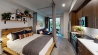 Located at 372 Fourth Ave in San Diego's Bankers Hill neighborhood, this single-floor studio unit offers a well-considered open-plan design that maximizes every inch of available space. The main living area flows seamlessly from the sleeping zone to the living and kitchen spaces, with floor-to-ceiling linen curtains on ceiling-mounted tracks providing a flexible, stylish partition between the bed and the lounge area. Rustic wood open shelving, warm-toned bedding, and botanical accents contribute to a curated, urban-bohemian aesthetic throughout.

The kitchen runs along one wall and is outfitted with rich walnut cabinetry extending to the ceiling, white subway tile backsplash, light quartz countertops, and a full suite of stainless steel appliances including a French door refrigerator, electric range with oven, built-in microwave, and a single-basin sink. Polished concrete-style flooring ties the kitchen and living areas together cohesively.

The bathroom features large-format gray tile flooring, a full soaking tub with white subway tile surround, a floating wood vanity with white countertop, and clean, neutral walls that create a bright, spa-like feel. A sliding mirrored closet door adds functionality while enhancing the sense of space. Natural light and outdoor greenery are visible through a glass door that opens to a private exterior area, bringing a refreshing connection to the outdoors.