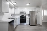 This single-story residence at 7557 W Florence Ln in Boise, Idaho presents a clean, updated interior with a straightforward and functional layout. The kitchen is a standout feature, showcasing white shaker-style cabinetry extending to the ceiling, a stainless steel appliance package including a refrigerator, electric range with overhead ventilation, and a double-basin sink. Light wood-look flooring and white tile-style backsplash contribute to the kitchen's bright, modern aesthetic, enhanced by flush-mount ceiling lighting.

The living areas feature light wood-look flooring and white-painted walls, creating an airy, neutral palette throughout. Windows fitted with horizontal blinds allow natural light to filter in while offering views of the surrounding greenery. A recessed window ledge in one room adds a subtle architectural detail and functional surface space.

The bedrooms are carpeted in a neutral tone, maintaining a warm and comfortable feel. At least one bedroom includes a sliding-panel closet with built-in shelving and a hanging rod, providing organized storage. The overall layout, as suggested by the 3D model, flows efficiently between living, kitchen, and sleeping areas, making practical use of the available footprint. The consistently neutral color scheme and updated finishes give the space a clean, move-in-ready appearance.