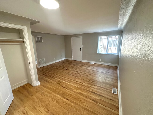 Bright room with elegant hardwood flooring, complemented by natural light streaming through large windows, creating a warm and inviting atmosphere. - Flats at 16th