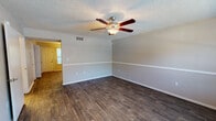 This two-floor space offers a functional and straightforward layout designed for comfortable everyday living. The main living area is a standout feature, showcasing dark hardwood-style flooring that runs throughout, neutral two-tone painted walls accented by a horizontal chair rail, a textured ceiling, and a ceiling fan with integrated lighting. A window allows natural light to filter in, offering views of surrounding greenery.

The kitchen is well-appointed with white cabinetry providing generous storage, dark granite-style countertops, a double sink, and a full suite of black appliances including a gas range, microwave, refrigerator, and dishwasher. Track lighting overhead ensures the space is well illuminated.

The bedrooms feature plush carpeting and neutral-toned walls, with windows dressed in blinds that frame outdoor views. Closet space is present, with at least one bedroom offering a walk-in style closet with built-in shelving.

The bathrooms are clean and practical, each featuring a full tub and shower combination with chrome fixtures, a toilet, and in one bathroom, a vanity with a mirror. The overall ambiance throughout is clean, neutral, and move-in ready.