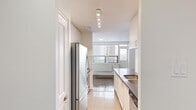 Located at 2222 Weston Rd, Suite 505 in Toronto's Weston neighbourhood, this two-bedroom, one-bathroom unit offers a practical and well-laid-out single-floor plan. The galley-style kitchen is outfitted with white cabinetry, dark countertops, stainless steel appliances including a full-size refrigerator and stove, a single-basin sink, and light tile flooring. Recessed track lighting runs along the ceiling, providing ample illumination. The kitchen opens directly into the living area, which features classic parquet wood flooring that extends throughout the main living spaces and bedrooms. Large windows in the living room allow natural light to fill the room and offer views of the surrounding cityscape, complemented by radiator heating units beneath each window. Both bedrooms are well-proportioned, each with parquet flooring, bright white walls, and windows with city views. The primary bedroom includes a set of double panel doors for closet access. The bathroom is finished with clean white subway tile surrounding a full soaking tub and shower combination, paired with chrome fixtures. A hallway connects the main rooms, creating a logical and functional flow throughout the unit.