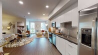 Located at 1101 N Main St in Los Angeles, CA, this single-floor residence offers a thoughtfully designed open-concept layout that seamlessly connects the kitchen, dining, and living areas. The kitchen is outfitted with sleek white cabinetry extending to the ceiling, dark countertops, a textured tile backsplash, and a full suite of stainless steel appliances including a range, over-the-range microwave, dishwasher, and a French door refrigerator. Wide-plank wood-style flooring runs throughout the main living areas, lending warmth and continuity to the space. The living room is bright and airy, benefiting from large floor-to-ceiling windows that invite generous natural light and provide views of the surrounding outdoor courtyard. A statement chandelier adds an elegant focal point overhead. The bedroom area is generously proportioned, accommodating a sitting space and a small dining area alongside the sleeping quarters, with direct access to a full bathroom. The bathroom features large-format tile flooring, a tub-shower combination with full tile surround, and clean, neutral finishes throughout. Recessed lighting and a well-considered layout enhance the functionality and comfort of this contemporary urban residence.