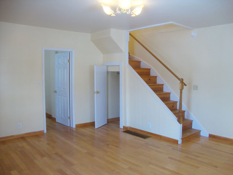 Living room with closet, entry to kitchen, and steps to second floor. - 239 W Venango St