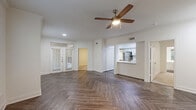 Located at 14885 Memorial Dr in Houston, TX, this single-floor residence offers two bedrooms and two full bathrooms in a thoughtfully designed layout. The living room makes a strong impression with its herringbone-patterned wood-look flooring, ceiling fan, crown molding, and multiple windows that bathe the space in natural light while offering views of surrounding greenery. The kitchen is a standout feature, showcasing white shaker cabinetry with gold hardware, a classic subway tile backsplash, white quartz countertops, stainless steel appliances, and a peninsula sink — all complemented by the same herringbone flooring that flows throughout the common areas. The primary bedroom is a comfortable retreat, carpeted for warmth, with a ceiling fan and access to a spacious walk-in closet outfitted with wire shelving on multiple walls. The second bedroom is similarly carpeted and bright. Both bathrooms are finished in a clean, all-white palette with soaking tub-shower combinations, wood-look tile flooring, and chrome fixtures. Two dedicated closets provide ample storage throughout. The overall aesthetic is modern and neutral, with consistent finishes creating a cohesive and inviting atmosphere throughout the home.