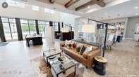 This generously sized single-floor space masterfully combines modern farmhouse aesthetics with contemporary design elements across its interconnected living, dining, and kitchen areas. The main living area commands attention with soaring ceilings accented by distinctive wood beam coffers, wide-plank hardwood flooring, and a striking feature wall that pairs dark shiplap with open walnut shelving. A chevron-tiled fireplace serves as a central focal point, while floor-to-ceiling black-framed windows flood the space with natural light and offer outdoor views.

The dining area showcases herringbone-tiled flooring, a warm wood-planked ceiling, and intimate built-in booth seating with upholstered benches and live-edge wood tables, each lit by a statement pendant. A secondary dining space provides ample seating around marble-topped tables, with direct access to an outdoor patio through large glass doors.

The kitchen features a long island with white quartz countertops, dark cabinetry, stainless steel appliances, decorative sconce lighting, and a detailed fan-pattern tile backsplash. A connecting hallway with plaid drapery and natural light ties all areas together seamlessly, creating a cohesive and inviting environment throughout.