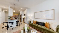 This single-floor residence showcases a thoughtfully designed open-concept layout with a clean, contemporary aesthetic throughout. The kitchen is a functional centerpiece, featuring stainless steel appliances including a refrigerator, range, and built-in microwave, complemented by white cabinetry extending to the ceiling, granite countertops, and light wood-style flooring that flows seamlessly through the main living areas. A breakfast bar with pendant lighting connects the kitchen to the rest of the living space.

The dining area is positioned adjacent to the kitchen and includes a built-in shelving niche, providing both storage and display space. The living room offers a comfortable, well-lit environment with natural light filtering through large windows dressed with blinds and drapes.

The bedrooms feature plush carpeting and windows that allow natural light, creating a calm and restful atmosphere. The bathroom is well-appointed with a soaking tub and shower combination featuring subway tile surround, a granite-topped vanity, and wood-style flooring. A dedicated in-unit laundry area with a full-size washer and dryer adds everyday convenience to this well-rounded residence.