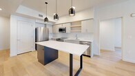 Located at 326 S 500 E in Salt Lake City, UT, this well-appointed 2-bedroom, 2-bathroom unit offers a thoughtfully designed single-level layout with a clean, contemporary aesthetic. Light hardwood flooring runs throughout the entire space, lending warmth and visual continuity to every room. The kitchen serves as a standout feature, showcasing a large center island with a striking white countertop and dark base, complemented by modern pendant lighting, gray flat-front cabinetry, open shelving, and a full suite of stainless steel appliances. The living area opens to a private balcony through a glass door, with windows framing elevated views of the Salt Lake City skyline. The primary bedroom is generously proportioned and includes a walk-in closet with dual hanging rods. Both bathrooms feature light hardwood flooring, modern gray vanities with white countertops, and clean white walls. One bathroom includes a glass-enclosed walk-in shower with a grab bar, while the other features a backlit vanity mirror for added ambiance. A connecting hallway ties the layout together efficiently. The overall design is minimal and bright, with neutral tones creating a calm, move-in-ready environment.