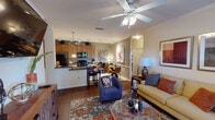 This single-story residence is designed with an open-concept layout that seamlessly connects the living, dining, and kitchen areas. Rich hardwood-style flooring flows throughout the main living spaces, complemented by crown molding and ceiling fans that lend a polished, cohesive aesthetic.

The living room is generously proportioned, featuring a ceiling fan with integrated lighting, a large area rug, and a glass-top coffee table. Natural light enters through a glass patio door, offering outdoor views, while framed artwork adorns the neutral-toned walls. The dining area sits adjacent to the kitchen, providing a smooth transition between spaces.

The kitchen is fully equipped with dark granite countertops, warm wood cabinetry extending to the ceiling, black appliances including a refrigerator, electric range, and built-in microwave, and tile flooring. Track lighting provides ample task illumination throughout.

The bedrooms feature plush carpeting, ceiling fans, and windows that allow natural light. One bedroom includes a dresser ensemble with wall sconces, adding a refined touch.

The bathrooms are finished with granite-topped vanities, wood cabinetry, tile flooring, and tub/shower combinations accented with coordinating tilework.