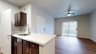 This single-floor residence offers a thoughtfully designed layout that balances functionality and comfort throughout. The open-concept living area serves as the heart of the home, featuring durable wood-style flooring, neutral-toned walls, and a ceiling fan with integrated lighting. A sliding glass door with vertical blinds fills the space with natural light and provides access to the outdoors. The kitchen is designed as a galley-style space and is outfitted with rich dark-stained cabinetry, white countertops, stainless steel appliances including a range, microwave, and refrigerator, and a deep single-basin sink with a flexible neck faucet. A peninsula counter connects the kitchen to the living area, offering additional workspace and casual seating potential. The bedrooms continue the wood-style flooring and are equipped with ceiling fans and windows fitted with horizontal blinds, allowing for natural light and ventilation. The full bathroom features a wide vanity with dark cabinetry, white countertops, a large mirror, and a shower-tub combination. A dedicated laundry room houses a full-size washer and dryer along with overhead shelving, adding a practical convenience to the residence.