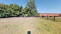 Located at 4187 Beechwold Dr in Columbus, Ohio, this single-level property presents itself as an open, fenced lot offering a blank canvas of usable outdoor space. The grounds are enclosed by a sturdy black metal fence, providing clear boundaries and a sense of security throughout the perimeter. The lot features an open grassy area that offers generous room for a variety of potential uses, bordered by mature, leafy trees that provide natural shade and a sense of privacy along the rear boundary. The lush tree line creates a natural green backdrop, enhancing the overall character of the space. A neighboring brick building is visible to the right, offering context for the surrounding residential neighborhood. The site benefits from an open sky exposure, allowing for abundant natural light across the grounds throughout the day. The interior spaces, as indicated by the floor plan, reflect a compact, single-story layout with a functional footprint. This property is well-suited for development, landscaping, or customization to meet a wide range of needs, and its location within an established Columbus neighborhood adds to its overall accessibility and appeal.