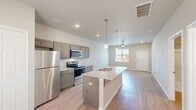 Located in Tyler, TX, this single-floor, 2-bedroom, 2-bathroom residence offers a thoughtfully designed open-concept layout. The kitchen and living area flow seamlessly together, anchored by a central island with a granite-style countertop, undermount sink, and stylish pendant lighting. Gray-toned cabinetry pairs with stainless steel appliances, including a refrigerator, electric range, and microwave, creating a contemporary and functional cooking space. Light wood-look flooring extends throughout the main living areas, complementing the neutral wall tones and recessed lighting. A ceiling fan adds comfort to the living room, which benefits from natural light streaming through a window overlooking the outdoors. Both bedrooms feature plush carpet flooring and windows with blinds, offering a quiet, comfortable retreat. The primary bedroom is a generous size, providing ample space for furnishings. The bathrooms include a full tub-and-shower combination with brushed nickel fixtures. Clean white walls, crisp trim work, and consistent finishes throughout lend the space a cohesive, move-in-ready feel. The front entry area, with its full window and solid door, provides a welcoming introduction to this efficiently designed home.