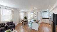 This single-floor residence is thoughtfully designed with an open-concept layout that seamlessly connects the kitchen, dining, and living areas. The kitchen is outfitted with stainless steel appliances, white cabinetry, recessed lighting, and a large island with a dark countertop that doubles as a breakfast bar with seating. Light wood flooring flows throughout the main living areas, enhancing the bright, airy atmosphere created by large windows and sliding glass doors.

The dining area comfortably accommodates a four-person table and benefits from natural light streaming through sheer curtains and a sliding door that opens to a private balcony with outdoor views. The living room features a neutral palette, a herringbone-patterned area rug, and ample space for relaxed seating.

The bedrooms are carpeted and equipped with ceiling fans, generous closet space, and natural light from window treatments. One bedroom includes a spacious walk-in closet with built-in shelving. Both bathrooms feature wood-look flooring, white cabinetry with grey countertops, and full soaking tubs with shower combinations. The overall ambiance is clean, modern, and welcoming throughout.