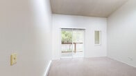 Located at 2380 NW Rolling Green Dr in Corvallis, Oregon, this single-floor residence offers a well-organized layout designed for comfortable everyday living. The living area is a standout feature, boasting soaring vaulted ceilings that amplify the sense of space and openness. Soft carpeting runs throughout, complemented by bright white walls and a large sliding glass door fitted with vertical blinds that opens to an outdoor deck area. Lush greenery is visible through the glass, bringing a natural element indoors. A secondary window alongside the sliding door adds additional natural light to the space. Baseboard heating is present throughout the unit, ensuring year-round comfort. The kitchen is equipped with essential appliances including an electric coil range, dishwasher, and full-size refrigerator. Wood-toned upper and lower cabinetry provides ample storage, while wood-look flooring adds warmth to the space. The bathroom features a full tub-shower combination, a wide vanity with generous counter space, and a large framed mirror illuminated by overhead pendant lighting. The bedroom is carpeted, with a textured ceiling and a window offering views of the surrounding greenery, providing a calm and restful atmosphere. The entry area transitions smoothly between the kitchen and living spaces, completing this functional and comfortable layout.