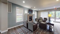 The Bridgewater Club Room is a thoughtfully designed single-floor community amenity space located in Bridgewater, NJ. The layout flows seamlessly across several functional zones, creating an inviting environment for socializing and recreation.

The main lounge area serves as the centerpiece of the space, featuring soft blue-gray walls, a tile-surround fireplace, and a wall-mounted flat-screen television above the mantle. Comfortable seating arrangements with upholstered chairs and sofas are grouped around glass-topped coffee tables, all set atop a richly patterned carpet with a geometric design in earth tones and blue accents. Recessed lighting and decorative wall sconces provide warm, ambient illumination, while large windows with roller shades flood the room with natural light and offer views of the surrounding greenery.

Adjacent to the lounge is a well-equipped kitchenette, finished with granite countertops, dark wood cabinetry, stainless steel appliances including a full-size refrigerator, and stone tile flooring — ideal for hosting gatherings and events.

A dedicated billiards area rounds out the space, offering a full-size pool table and additional wall-mounted television, providing an entertaining retreat for residents. Transitional hallways connect the zones with console furnishings and decorative accents, contributing to a cohesive and polished overall aesthetic.