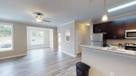 This single-floor unit features a well-designed open-concept layout that connects the kitchen and living areas seamlessly. The living space is finished with light gray wood-look flooring and neutral-toned walls, crowned with decorative molding and a ceiling fan. Multiple windows with blinds allow natural light to fill the space, offering views of the surrounding neighborhood.

The kitchen is well-appointed with dark espresso cabinetry, granite-look countertops, and a full suite of stainless steel appliances, including a refrigerator, range, and microwave. A peninsula with pendant lighting overhead serves as both a workspace and a casual dining area. Tile flooring extends throughout the kitchen, contrasting with the wood-look floors in the adjacent living areas.

The unit includes multiple bedrooms, each featuring the same wood-look flooring and ample natural light from large windows. A spacious walk-in closet provides generous storage with wire shelving. Two bathrooms are finished with dark vanity cabinetry, granite-look countertops, and tile flooring, with one featuring a shower-tub combination. The overall ambiance is clean, modern, and functional.