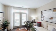 Located at 700–712 E North St in Indianapolis, Indiana, this single-story residence offers a thoughtfully designed layout with a cohesive, contemporary aesthetic throughout. The living area serves as the heart of the unit, featuring wood-style flooring, neutral-toned walls, and a set of French doors that invite abundant natural light while providing access to an outdoor area with views of the surrounding brick exterior. Sheer drapery panels frame the doors, contributing to a bright and airy atmosphere. The kitchen is efficiently arranged with light maple cabinetry extending to the ceiling for ample storage, dark countertops, wood-style flooring, and a full suite of black appliances including a range, microwave, dishwasher, and refrigerator. A kitchen island provides additional prep and counter space. The bedroom features plush carpeting, a generously sized window with exterior views, and neutral walls that create a calm, restful environment. The bathroom is finished with a floating wood vanity, dark countertop, a large mirror, wood-style tile flooring, and a shower-tub combination, maintaining the consistent design language found throughout the unit.