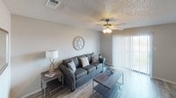 This single-floor residence offers a thoughtfully designed layout that balances comfort and functionality across a variety of well-defined living spaces. The living room serves as the heart of the home, featuring wood-look flooring, a ceiling fan with integrated lighting, and vertical blinds that open to allow natural light to fill the room. The neutral gray tones and understated décor create a calm, welcoming atmosphere.

Adjacent to the living area, a dedicated dining space provides room for a round table and chairs beneath a pendant light fixture, with wood-look flooring continuing throughout. A framed chalkboard wall accent adds a casual, personalized touch. The galley-style kitchen is efficiently organized, featuring gray cabinetry on both sides, light countertops, a stainless steel sink, and white appliances including a range, microwave, and refrigerator.

The primary bedroom stands out with stylish sliding barn doors that provide access to the closet, blending farmhouse character with practical storage. A second bedroom offers a softer aesthetic, with carpet flooring, gray curtains filtering natural light, and wall art above a upholstered headboard. The bathroom is clean and modern, with a white-framed vanity mirror, a three-bulb light fixture, gray cabinetry, and light countertops. Textured ceilings are consistent throughout the residence.
