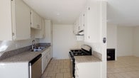 Located at 13990 Astoria St in the Sylmar neighborhood of Los Angeles, this single-story unit offers a practical and functional layout across its living spaces. The galley-style kitchen is well-appointed with white cabinetry offering ample upper and lower storage, granite-patterned countertops, a stainless steel sink with dishwasher, and a black gas range with overhead ventilation. Light tile flooring runs throughout the kitchen, giving it a clean, bright appearance. The open living and dining area features the same light tile flooring, a textured ceiling, and a fireplace that serves as a focal point, adding warmth and character to the space. Natural light filters in generously, enhancing the airy feel of the room. The bedrooms are finished with wall-to-wall carpeting and feature windows dressed with vertical blinds, allowing for adjustable natural light. One bedroom includes a sliding glass door that opens to an outdoor area, further expanding the sense of space. The bathroom is equipped with a full-size tub and shower combination enclosed by sliding glass doors, complemented by tile flooring, a toilet, and a vanity with sink. Overall, the unit presents a clean, neutral palette throughout.