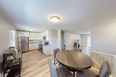 Located at La Bonne Vie in East Patchogue, NY, this two-story, one-bedroom, one-bathroom residence is thoughtfully designed to maximize comfort and functionality. The main floor hosts the majority of the living space, featuring light hardwood-style flooring throughout the open-concept layout. The kitchen is well-appointed with white shaker cabinetry, granite countertops, stainless steel appliances including a refrigerator and dishwasher, and a classic subway-tile-style backsplash. A dedicated dining area flows naturally from the kitchen into the spacious living room, which is illuminated by recessed lighting and features a sliding glass door that brings in natural light and provides outdoor access. The bedroom is a comfortable retreat finished with plush carpeting, a ceiling fan, natural window light, and a closet. An additional closet provides extra storage. The full bathroom features a tiled tub-shower combination with a curved curtain rod and granite vanity countertop. A staircase with light wood treads and white risers connects the lower entry level to the main floor above, completing the two-story layout of this well-maintained East Patchogue residence.