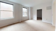 Located at 101 W Read St in Baltimore's vibrant Mount Vernon neighborhood, this single-floor unit offers a thoughtfully laid-out interior with a clean, neutral aesthetic throughout. The generously sized living area is finished with plush wall-to-wall carpeting and crisp white walls, creating a bright and inviting atmosphere. Multiple double-hung windows allow natural light to filter in, with views of the surrounding urban streetscape. A pass-through opening connects the living space to the kitchen, enhancing the sense of openness and flow. The galley-style kitchen is well-appointed with light wood cabinetry, dark countertops, and hardwood-style flooring, providing ample counter and storage space along both sides of the corridor. A stainless range anchors one end of the kitchen, making it both functional and practical. The bedroom is carpeted and generously proportioned, with large windows that continue the theme of natural light, and access to a dedicated closet space. The full bathroom features classic penny-tile flooring in a neutral tone, a wood-vanity with a single sink, a large mirror, and clean, understated finishes throughout. The overall ambiance is calm and move-in ready, well-suited for urban living in the heart of Baltimore.