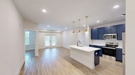 Located in Charleston, SC, this thoughtfully designed 3-bedroom, 2-bathroom single-story home offers a clean, modern aesthetic throughout. The kitchen serves as a striking centerpiece, showcasing bold navy blue shaker-style cabinetry accented with gold hardware, crisp white quartz countertops, a white subway tile backsplash, and a full suite of stainless steel appliances. A central island with pendant lighting adds both functionality and style to the space. Light-toned hardwood flooring flows seamlessly throughout the entire home, contributing to a bright and cohesive feel. The open living area features recessed lighting and a set of French doors that invite natural light and provide outdoor access. Each of the three bedrooms offers a calm, neutral palette with ample natural light from well-placed windows. The primary bedroom connects to a dedicated bathroom finished with navy vanity cabinetry, gold hardware, a white countertop, and a large framed mirror, with direct access to a walk-in closet equipped with wire shelving systems. A second full bathroom mirrors the same refined design language. Three total closets provide generous storage throughout the home, completing this well-appointed Charleston residence.