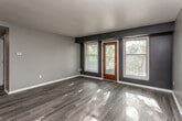 This single-story residence offers a well-organized layout with a cohesive, modern aesthetic carried throughout. The galley-style kitchen is outfitted with white shaker cabinetry accented by matte black hardware, light countertops, a subway tile backsplash, stainless steel refrigerator, and matching appliances — delivering a clean, functional workspace. The kitchen opens toward the living area, which features dark hardwood-style flooring and a bold accent wall, lending depth and visual contrast to the space. A ceiling fan overhead and a set of windows alongside a wood-framed glass door bring in natural light and provide access to an outdoor area.

A secondary room adjacent to the living space includes stacked in-unit washer and dryer units, a dark accent wall, and continued hardwood-style flooring — a practical and convenient feature. The bedrooms are finished with plush carpeting in a neutral tone, gray walls, and individual windows that allow natural light. At least one bedroom includes a walk-in closet with built-in rod storage. The bathroom features a full soaking tub with a shower surround and brushed nickel hardware. Throughout the unit, consistent gray tones, white trim, and dark flooring create a cohesive, contemporary feel.