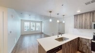Unit 254 at 308 W North Temple in Salt Lake City is a 910-square-foot, single-story apartment offering two bedrooms and two bathrooms. The open-concept kitchen and living area forms the heart of the unit, where light wood-style flooring extends throughout the main space. The kitchen is equipped with stainless steel appliances—including a refrigerator, range, and microwave—complemented by dark wood-tone cabinetry and white quartz countertops. A large island with an undermount sink and pendant lighting above serves as a functional centerpiece, seamlessly connecting to the living area. The living room receives abundant natural light through a set of large windows fitted with horizontal blinds, offering views of the surrounding community. The primary bedroom measures 180 square feet and features a ceiling fan, carpeted flooring, and a window. The second bedroom is similarly carpeted with a window providing natural light and includes access to a dedicated closet. Both bathrooms are finished with wood-tone vanities, quartz countertops, and light wood-style flooring; one bathroom includes a full tub-shower combination. Neutral tones and clean finishes give the entire unit a modern, cohesive aesthetic.