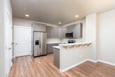 Located at 4400 Briggs Dr SE in Olympia, Washington, this well-appointed two-story home offers a thoughtfully designed layout with modern finishes throughout. The main living area features warm hardwood-style flooring and an open flow between the living and dining spaces, where a chandelier adds an elegant focal point and large windows fitted with blinds invite generous natural light. The kitchen is outfitted with contemporary flat-front cabinetry in a warm gray wood finish, light quartz countertops, and a full suite of stainless steel appliances including a refrigerator, electric range, built-in microwave, and a stainless undermount sink. A dedicated laundry room houses a side-by-side washer and dryer set, complemented by overhead cabinetry and a folding counter for added convenience. The bedrooms are carpeted for comfort and include closet storage, with natural light filtering through window blinds. The bathrooms are finished with wood-toned vanity cabinetry, quartz countertops, and undermount sinks. One bathroom features a shower-tub combination with tile surround, while another offers a walk-in shower. The home's neutral color palette and clean architectural lines create a bright, cohesive living environment throughout both floors.
