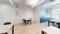 Located at 13857 E Arapahoe Pl in Centennial, Colorado, this art studio is a thoughtfully designed single-room space that balances functionality with a clean, modern aesthetic. The interior features light hardwood flooring throughout, white walls, and linear pendant lighting that ensures consistent, well-distributed illumination across the entire room — ideal for detail-oriented creative work.

The studio is arranged to accommodate multiple workgroups simultaneously, with several rectangular tables and black chairs distributed throughout the space. A large window along one wall floods the room with natural light and offers views of the surrounding Centennial neighborhood. Adjacent to the window, a floor-to-ceiling modular shelving unit provides ample organized storage with labeled bins, keeping supplies accessible and the workspace tidy.

A built-in cabinetry station with a sink and countertop runs along one side of the room, outfitted with teal-blue lower cabinets and a light countertop — a practical utility area for art-related tasks requiring water access. An additional storage unit with open cubbies and matching bins adds further organizational capacity.

The layout is open and flexible, with clear sightlines across the room and sufficient circulation space between workstations. Signage on the wall outlines studio rules, reinforcing the space's role as a shared, community-oriented creative environment. Overall, the studio presents a bright, orderly, and welcoming setting well-suited for structured art programming.