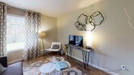 This single-floor residence in Tacoma, Washington offers a well-organized layout across several distinct living areas. The living room serves as a central gathering space, featuring a tile-surround fireplace, wood-look flooring, and room for comfortable seating arrangements. Decorative wall art and layered lighting contribute to a warm, inviting ambiance throughout.

Adjacent to the living room, the dining area accommodates a round table and chairs beneath a ceiling fan with integrated lighting. A pass-through connects this space to the kitchen, which is equipped with light wood cabinetry, white countertops, a black electric range with stainless steel range hood, and a full-size refrigerator. The open sightlines between the dining and kitchen areas create a cohesive, functional flow.

The bedroom features soft carpet flooring, a mirrored sliding closet, and a window dressed with sheer curtains and blinds that allow natural light while maintaining privacy. The bathroom includes a tub-shower combination with a curtain rod, wood-look vinyl flooring, and neutral wall tones. A dedicated laundry closet houses a full-size washer and dryer side by side, with overhead cabinetry providing additional storage.