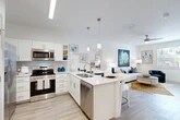 Located in Gainesville, FL, this well-designed 2-bedroom, 2-bathroom residence offers a bright, modern living experience across a single floor. The open-concept living, dining, and kitchen area serves as the heart of the home, anchored by a large center island with bar seating and elegant pendant lighting overhead. The kitchen is outfitted with stainless steel appliances, white shaker cabinetry, and light quartz countertops, all complemented by wood-style plank flooring that flows throughout the space. The living area benefits from abundant natural light and a ceiling fan, creating a comfortable, airy atmosphere. The primary bedroom features French doors opening to an outdoor balcony, offering pleasant outdoor views, and is equipped with a walk-in closet accessed through a stylish sliding barn door. The en-suite primary bathroom includes a vanity with ample cabinet storage and a glass-enclosed tiled shower. The second bedroom provides a versatile space with natural light from large windows. The second bathroom features a tiled tub-shower combination and a white vanity. A dedicated in-unit laundry room with a full-size washer and dryer adds everyday convenience, while a utility room provides additional storage. The clean, neutral palette and modern finishes give the entire residence a cohesive, contemporary feel.