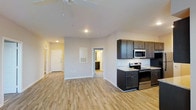 Unit 202 is a two-bedroom, two-bathroom single-floor residence designed with an open-concept layout that seamlessly connects the main living areas. Light hardwood-style flooring extends throughout the space, contributing to a clean, cohesive aesthetic that enhances the sense of openness.

The kitchen is positioned along one wall and features dark espresso-toned cabinetry that provides strong visual contrast against the light-colored countertops and neutral walls. Stainless steel appliances, including an electric range and over-the-range microwave, offer a modern, functional finish. A tile backsplash adds a refined detail to the cooking area.

The open living area flows naturally from the kitchen, offering flexible space for dining and lounging. A ceiling fan is installed overhead, providing both air circulation and ambient lighting. The entryway is clearly defined with a solid front door and access panel, while a hallway leads to additional rooms, including what appears to be a bathroom visible in the background. The overall ambiance is bright, neutral, and move-in ready, with a straightforward layout that maximizes usable space.