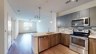 Located on Martin Luther King Jr Drive SE in Atlanta, Georgia, this single-floor unit presents a contemporary open-concept design that seamlessly connects the kitchen and living areas. The kitchen is a standout feature, equipped with stainless steel appliances including a range, microwave, and dishwasher. Two-toned cabinetry pairs warm wood lower cabinets with sleek slate-blue upper cabinets, accented by a tile backsplash. A peninsula with a built-in sink and light countertops provides additional prep space and serves as a natural divider between the kitchen and the open living area. Pendant lighting and a track light fixture illuminate the kitchen, while a ceiling fan services the living space beyond.

Wood-look flooring flows throughout the main living and kitchen areas, creating a cohesive, modern aesthetic. The bedrooms feature plush carpeting and receive natural light through windows that frame views of the surrounding Atlanta cityscape and greenery. A generously sized walk-in closet with wire shelving and carpeted flooring offers substantial storage. A dedicated hallway connects all areas of the unit, contributing to a functional and well-organized layout overall.