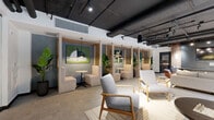 Located at 49 Fisk St in Jersey City, NJ, this thoughtfully designed amenity lounge offers a sophisticated blend of industrial and contemporary aesthetics across a single, expansive floor. The space features exposed ceilings with visible ductwork and black-painted structural elements, offset by warm track lighting and pendant fixtures that create an inviting, well-lit atmosphere throughout.

The open layout is divided into distinct functional zones. A lounge area anchors the space with plush sofas, mid-century modern armchairs in neutral tones, and low coffee tables arranged atop area rugs. Floor-to-ceiling windows flood this zone with natural light and provide views of the surrounding courtyard. Adjacent to the lounge, a media wall finished in dark concrete-toned panels features a mounted flat-screen TV, built-in shelving, and rich wood cabinetry accents.

Semi-private booth seating areas, framed by warm wood slat partitions and adorned with vibrant artwork and lush tropical plants, offer intimate settings ideal for focused work or conversation. Glass partition walls define additional zones while maintaining visual openness throughout. Consistent large-format tile flooring in a soft gray palette unifies the entire space, complementing the refined yet relaxed character of this well-appointed communal lounge.
