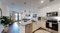 Located at 44 Braves Ave in Lawrenceville, Georgia, this single-floor residence offers a thoughtfully designed open-concept layout that seamlessly connects the kitchen, dining, and living areas. The kitchen is a standout feature, equipped with sleek white cabinetry, granite countertops, a large center island with a stainless steel sink and dishwasher, and a full suite of stainless steel appliances including a range, microwave, and refrigerator. Three polished pendant lights hang above the island, adding a refined touch to the space. A classic white subway tile backsplash completes the kitchen's clean, modern aesthetic. Rich hardwood-style flooring flows throughout the main living areas, grounding the bright, airy interior. The living room is bathed in natural light from large French doors that open to an outdoor area, and a ceiling fan overhead enhances comfort. The bedroom features a large window with abundant natural light, patterned accent wallpaper, and a cozy, well-appointed atmosphere. The bathroom offers a granite-topped vanity, wood-style flooring, and a well-lit mirror setup. Throughout the residence, bold dark-painted interior doors provide a striking contrast against the crisp white walls, lending the space a contemporary and polished character.