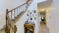 The first floor of this two-storey home offers a thoughtfully arranged layout that balances functionality with comfort. A central hallway connects the various living areas, creating a natural flow throughout the space. The staircase serves as a notable architectural feature, finished with warm wooden balusters and a turned newel post, complemented by carpeted treads that add a classic, homey touch. The adjacent wall is adorned with a curated gallery of framed photographs and decorative lettering, lending the entryway a personal and welcoming character.

The hallway extends toward the rear of the home, where carpeted rooms offer comfortable living and sleeping areas. From the 3D floor plan, the first floor includes what appears to be a bedroom with a dedicated sleeping area, along with additional rooms that provide flexible living arrangements. Bright, neutral wall tones are consistent throughout, contributing to an open and airy atmosphere. Interior doors and trim are finished in crisp white, enhancing the clean aesthetic. Natural light filters in through windows visible toward the back of the hallway, adding warmth and brightness to the overall environment.