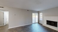 Located at 6317 Shanda Dr in Raleigh, NC, this two-bedroom, one-bathroom single-story home offers a practical and comfortable layout. The combined kitchen and living area serves as the heart of the home. The living room features dark hardwood-style flooring, neutral gray walls, and a classic white brick wood-burning fireplace flanked by sliding glass doors and windows that allow ample natural light and provide direct access to a private patio with outdoor views. The galley-style kitchen is well-appointed with white cabinetry, light countertops, track lighting set into a tray ceiling, and black appliances including a refrigerator, stove, and dishwasher, all complemented by light wood-tone flooring. The primary bedroom is generously sized, finished with plush carpet, and includes both a standard closet and a dedicated walk-in closet outfitted with built-in shelving and hanging rods. The second bedroom also features carpet flooring and neutral tones, with its own sliding glass door opening to the patio. The full bathroom includes a tub-shower combination with built-in shelving. A hallway connects the main living spaces, completing this efficient and well-designed floor plan.