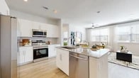 This thoughtfully designed 2-bedroom, 2-bathroom residence offers a bright, open-concept floor plan that seamlessly connects the kitchen, dining, and living areas. The modern kitchen serves as the centerpiece of the home, showcasing white shaker-style cabinetry, granite countertops, a large central island with bar seating, and a full suite of stainless steel appliances including a side-by-side refrigerator, range, microwave, and dishwasher. Neutral-toned subway tile backsplash and light wood-style vinyl flooring carry throughout the space, creating a clean and cohesive aesthetic. The open living area benefits from abundant natural light through large windows dressed with blinds and curtain panels, and features a ceiling fan for added comfort. Both bedrooms are generously sized, with the primary bedroom offering a ceiling fan, large windows, and access to a dedicated walk-in closet equipped with wire shelving. Each of the two bathrooms is finished with white cabinetry and tiled tub-shower combinations. A second closet provides additional storage. The consistent use of light tones, recessed lighting, and contemporary finishes throughout gives this residence a modern, move-in-ready appeal.