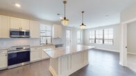 Located at 1550 Kenny Rd in Columbus, Ohio, this thoughtfully designed single-floor residence offers a seamless blend of modern finishes and functional living spaces. The open-concept kitchen and living area serves as the heart of the home, anchored by a substantial center island topped with light granite countertops and illuminated by a pair of brass-finished schoolhouse pendant lights. White shaker cabinetry lines the kitchen walls, complemented by a decorative arabesque tile backsplash and a full suite of stainless steel appliances, including a French door refrigerator, range, microwave, and dishwasher. Rich hardwood flooring flows throughout the main living areas, connecting the kitchen to a bright, expansive living room bathed in natural light from large windows and a glass door that opens to an outdoor area. The bedroom features plush carpeting, a decorative wainscoting accent wall, and a generously sized walk-in closet with multi-tiered shelving and hanging rods. The primary bathroom is appointed with a granite-topped vanity, patterned hexagonal tile flooring, dark subway tile wall accents, and matte black hardware, adding a sophisticated contrast. Direct access from the bathroom to the walk-in closet enhances the suite's practicality and flow.