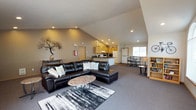Located at 2808 South Assembly Road in Spokane, Washington, this single-floor space offers an open and functional layout designed for comfort and practicality. The interior is characterized by soaring vaulted ceilings that lend an airy, expansive feel throughout the main living area, which is anchored by plush carpeting and recessed lighting. Large windows allow abundant natural light to flood the space, enhancing the welcoming atmosphere.

The living area is generously proportioned, providing ample room for seating and gatherings, and flows seamlessly into the kitchen and dining zones. The kitchen is well-appointed with light oak cabinetry, dark granite-style countertops, a breakfast bar peninsula, and white appliances including a range, refrigerator, and dishwasher. Tile flooring in the kitchen offers a clean contrast to the carpeted living spaces.

A secondary lounge or multipurpose room features arched windows, neutral walls, and additional recessed lighting, making it a versatile space suited for a variety of uses. Decorative wall accents and thoughtful furnishings contribute to the space's warm, inviting character. The overall design is straightforward and functional, with a neutral color palette that makes the space adaptable for residential, community, or event use.