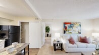 Located on Executive Drive NW in Huntsville, Alabama, this well-appointed one-bedroom, one-bathroom unit offers a thoughtfully designed single-floor layout. The living room serves as the heart of the space, featuring warm neutral-toned carpet, a large window that frames lush greenery views, and an open, inviting ambiance complemented by bold abstract artwork on the walls. The kitchen is equipped with classic white cabinetry, a double-basin sink, wood-look flooring, and black appliances including a full-size refrigerator and range, providing a clean and functional cooking space. The spacious primary bedroom is generously sized, featuring plush carpeting, multiple windows that flood the room with natural light and outdoor views, and ample space for a full furniture arrangement. A dedicated closet offers convenient storage. The full bathroom includes a tiled tub-shower combination, maintaining a clean, bright aesthetic throughout. Neutral warm tones carry consistently through every room, creating a cohesive and comfortable atmosphere. This efficiently organized unit makes excellent use of its footprint, offering a practical and comfortable living environment in Huntsville's northwest corridor.