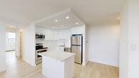 Located at 2150 Roche in Mississauga, Ontario, this well-appointed unit offers a clean, modern aesthetic throughout its single-floor layout. The renovated kitchen serves as a standout feature, showcasing high-gloss white cabinetry that extends to the ceiling, sleek light-toned quartz countertops, and a full suite of stainless steel appliances including a refrigerator, electric range, built-in microwave, and dishwasher. A central island provides additional prep space and anchors the kitchen's open layout. Light-toned hardwood flooring flows consistently throughout the unit, lending warmth and visual continuity to every room. The living area is generously proportioned, with large windows that allow ample natural light and frame views of the surrounding Mississauga landscape. Multiple bedrooms offer comfortable dimensions, each benefiting from windows with outdoor views and baseboard heating. One bedroom includes a walk-in closet with built-in shelving, adding practical storage. The overall design palette is bright and neutral, with white walls and clean lines creating a fresh, contemporary atmosphere. Recessed lighting in the kitchen adds a polished finishing touch, making this unit a well-rounded and functional living space in an established Mississauga location.