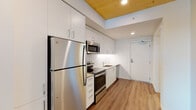 Located at 1090 NE 91st Ave in Hillsboro, Oregon, this single-floor unit offers a thoughtfully designed layout with modern finishes throughout. The kitchen is a standout feature, showcasing a full suite of stainless steel appliances including a refrigerator, electric range, over-the-range microwave, and dishwasher. Crisp white cabinetry extends floor to ceiling, providing generous storage, while a white subway tile backsplash and clean countertops complete the contemporary aesthetic. Warm wood-look luxury vinyl plank flooring runs throughout the unit, adding a welcoming contrast to the bright white walls. A distinctive natural wood-paneled ceiling adds warmth and architectural character to the kitchen and living areas. The bedroom is generously sized, featuring the same wood-paneled ceiling, a ceiling fan with light fixture, and a window that brings in natural light with views of the surrounding greenery. A walk-in closet with built-in shelving provides excellent organization and storage space. The bathroom is finished in a neutral palette with a single-sink vanity, wall-mounted storage cabinet, a large mirror, and durable wood-look flooring. Accessibility-friendly grab bars are thoughtfully incorporated. The unit's clean, modern design and functional layout make it a comfortable and practical living space.