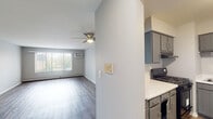 Located at 561 Deere Park Cir in Bartlett, IL, this single-floor unit offers a practical and well-maintained layout across several distinct living areas. The open living room is a bright, inviting space featuring durable wood-style plank flooring, a ceiling fan with light fixture, a large window that allows generous natural light, a wall-mounted air conditioning unit, and baseboard heating for year-round comfort. Adjacent to the living area, the kitchen is efficiently designed with gray shaker-style cabinetry, light countertops, a stainless steel sink, a gas range with overhead ventilation, and a full-size black refrigerator — providing all essential appliances in a compact, functional arrangement. The bedroom is a comfortably sized, carpeted room with its own window and wall-mounted air conditioner, creating a quiet and cozy retreat. A separate room with wood-style flooring includes a tall built-in wardrobe with ample storage and provides access to additional areas of the unit. The bathroom is neatly appointed with a tiled tub-shower combination, a white vanity with sink, a mirrored medicine cabinet, and overhead lighting, offering a clean and functional space. Throughout, neutral gray walls and consistent finishes create a cohesive, move-in-ready atmosphere.